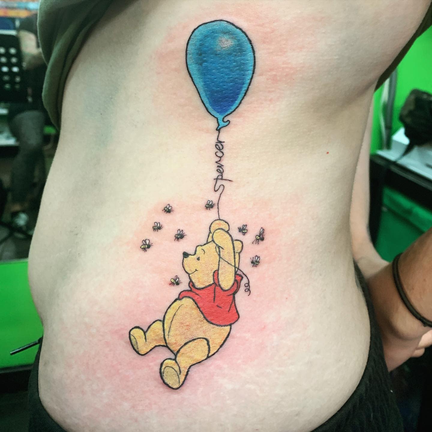 Winnie the Pooh tattoo holding a blue balloon with bees around on side
